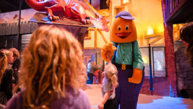 Kinderen spelen in de nieuwe binnenspeeltuin Drakendorp van BillyBird Drakenrijk, met het brandende middeleeuwse dorp en de grote draak op de achtergrond.